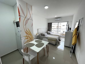A modern hotel room with a bed, a desk, and a dining area.