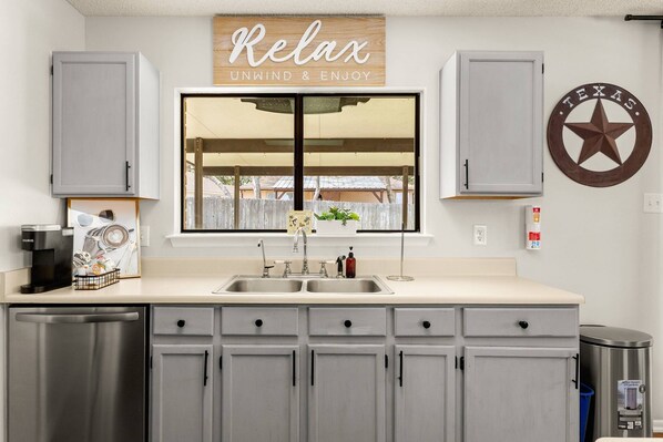 A kitchen with grey cabinets, a double sink, a coffee maker, and a star-shaped wall decoration.