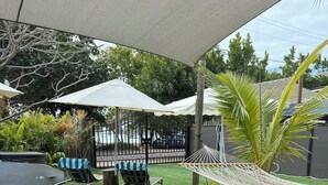 An outdoor patio with a wooden table, wicker chairs, and a hammock.