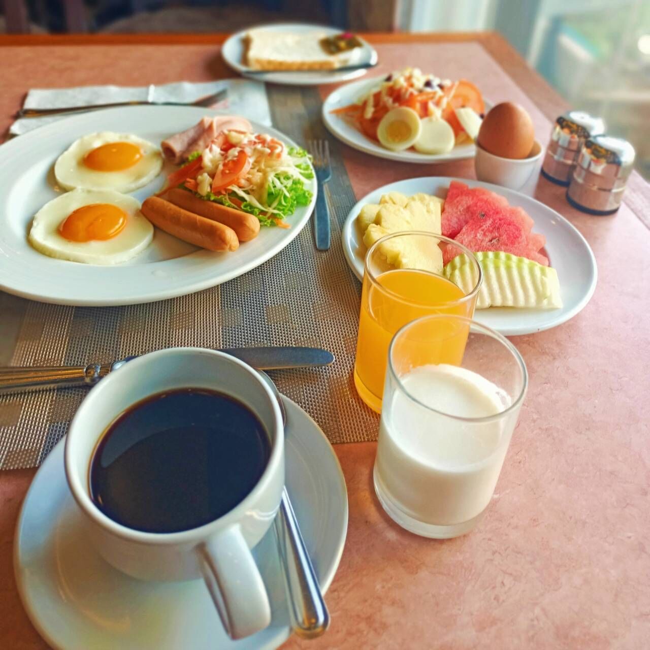 A breakfast setting with plates of eggs, sausages, and vegetables, along with a cup of coffee and a glass of orange juice.