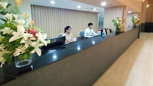 Un mostrador de recepción con dos empleados, un interior moderno y arreglos florales decorativos.