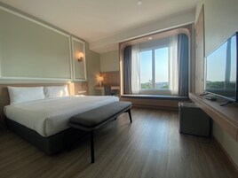 Una habitación de hotel con una cama grande, un escritorio, un televisor y una ventana con cortinas.