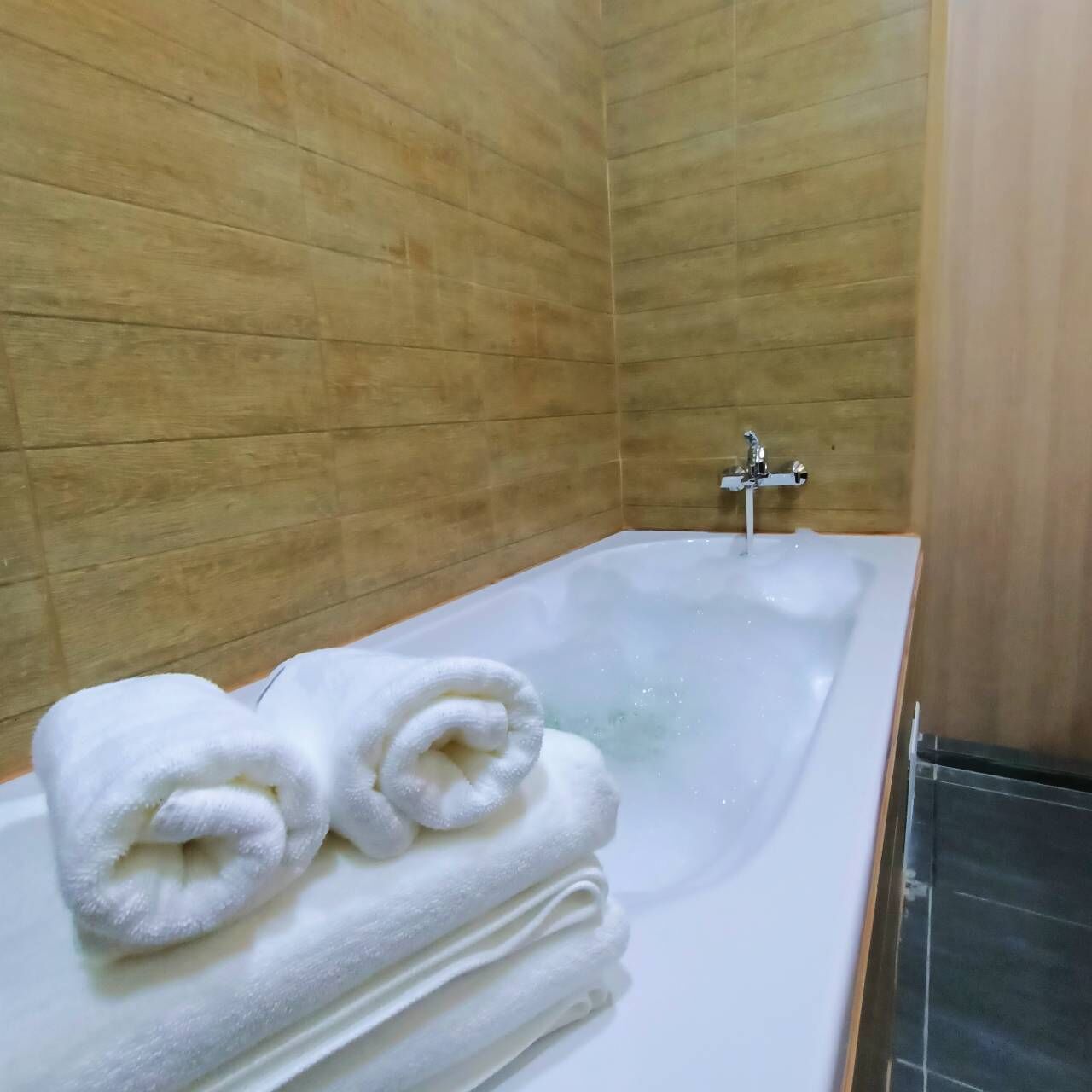 Un baño con bañera, paredes de madera y dos toallas enrolladas al borde.