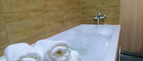 Un baño con bañera, paredes de madera y dos toallas enrolladas al borde.