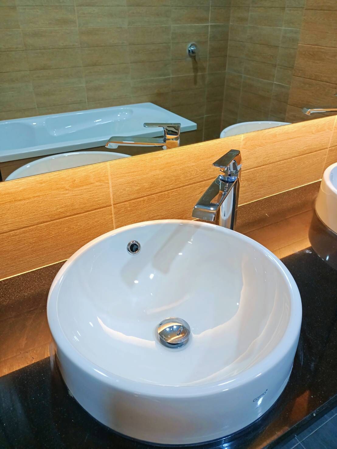 A bathroom with a white sink, a chrome faucet, and a mirror reflecting a toilet and a bathtub.