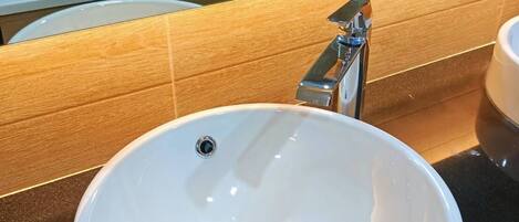 A bathroom with a white sink, a chrome faucet, and a mirror reflecting a toilet and a bathtub.