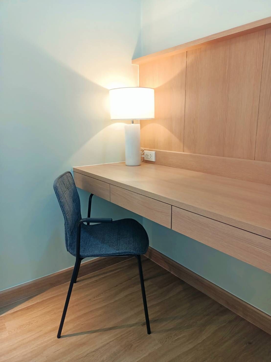 Un petit espace de travail moderne, comprenant un bureau et une chaise, une lampe et un mur en bois.