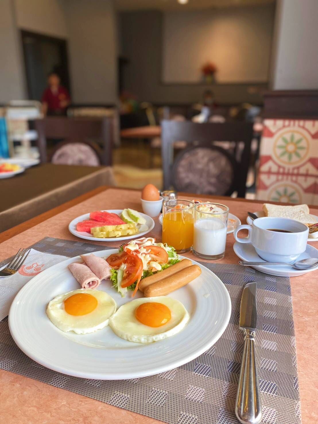A breakfast setting with eggs, sausages, and a salad on a plate, accompanied by a glass of orange juice and a cup of coffee.