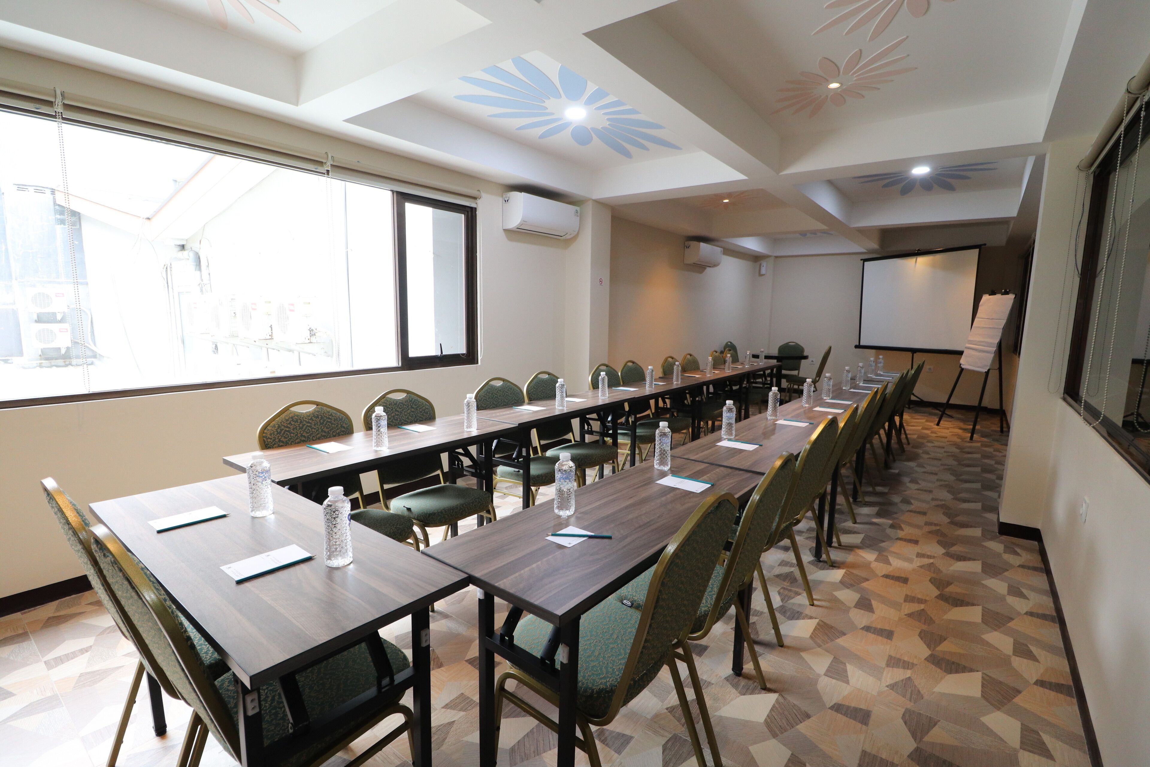 A conference room with a long table, chairs, a projector screen, and a large window.
