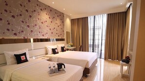 Una habitación de hotel con dos camas, un escritorio, una silla y un ventanal con cortinas.
