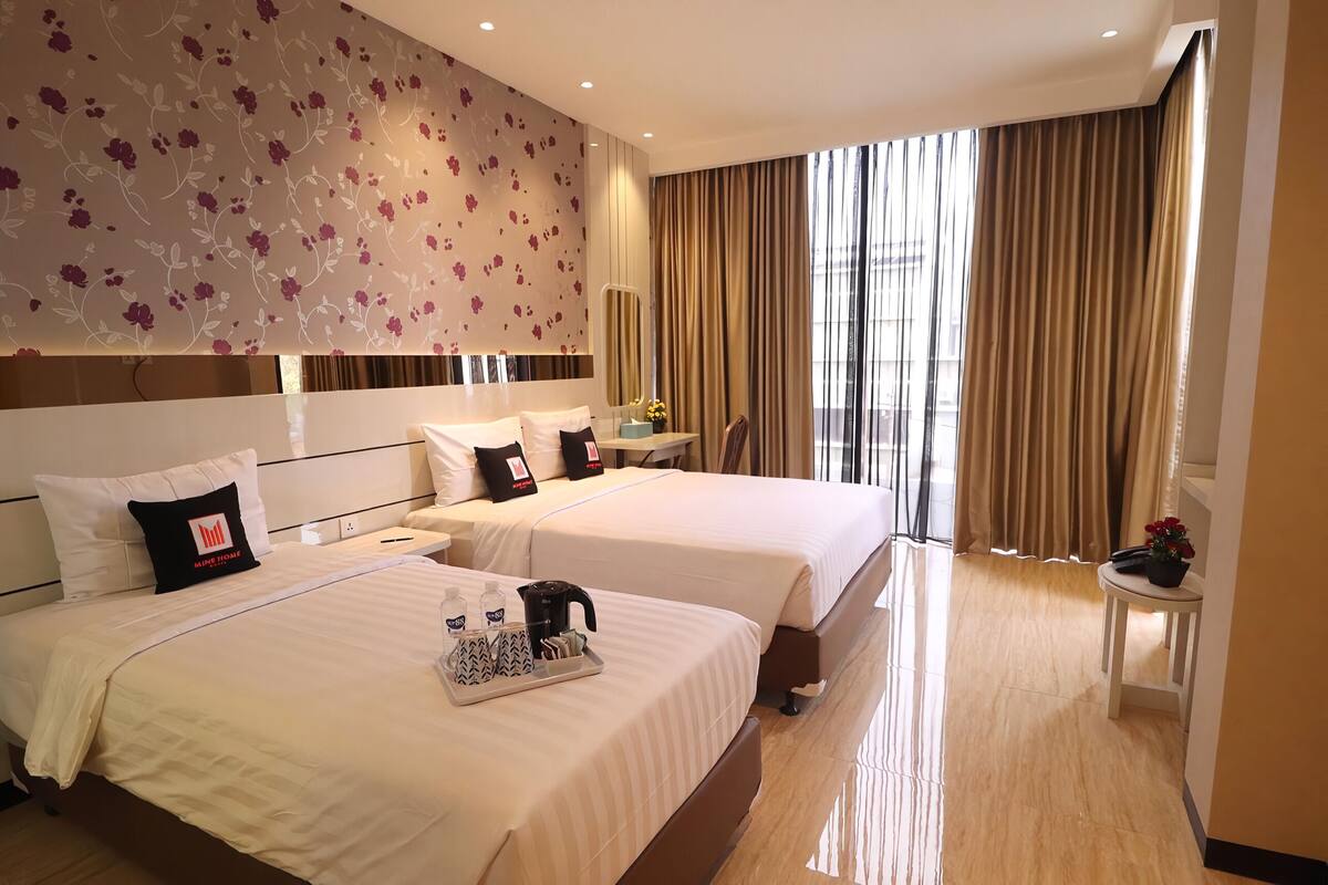 A hotel room with two beds, a desk, a chair, and a large window with curtains.