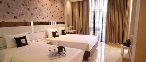 Una habitación de hotel con dos camas, un escritorio, una silla y un ventanal con cortinas.