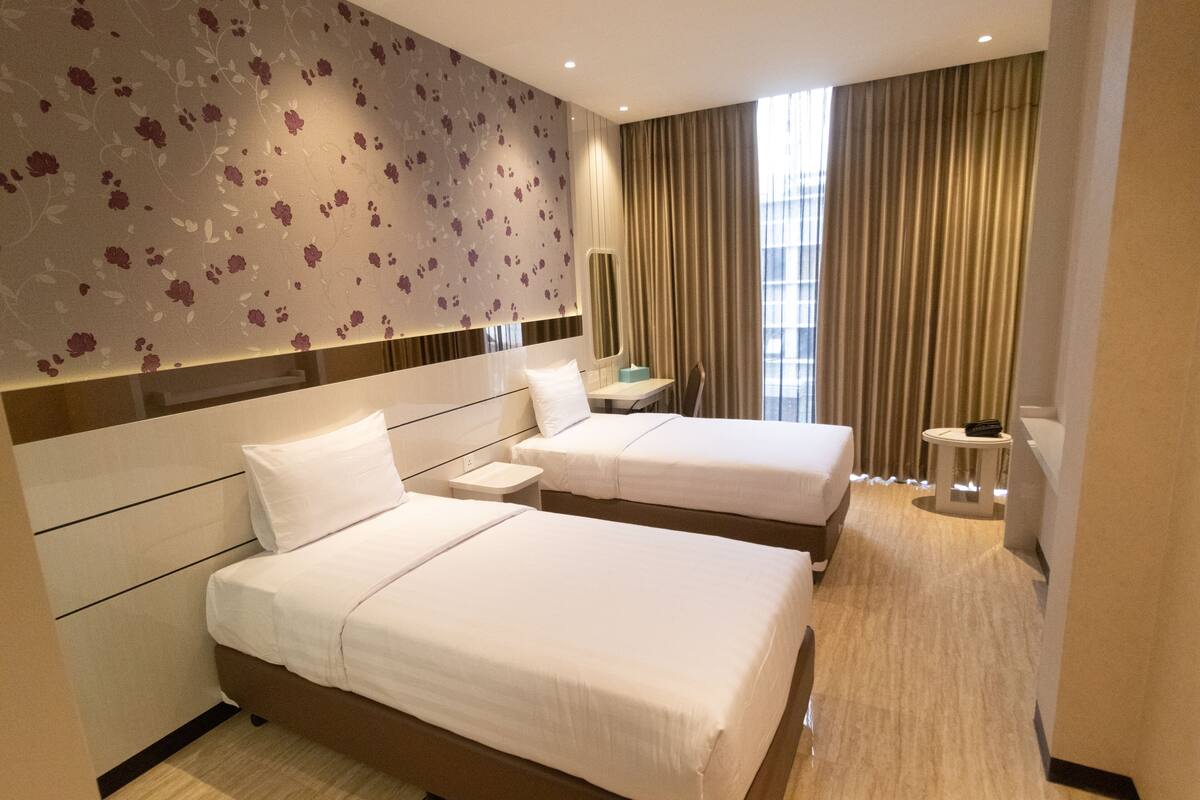A hotel room with two beds, a mirror, a small table, and a view of the city through large windows.