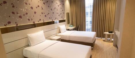 A hotel room with two beds, a mirror, a small table, and a view of the city through large windows.