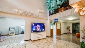 Un vestíbulo con suelo de mármol, un televisor de pantalla plana sobre un mueble blanco y un reloj en la pared.