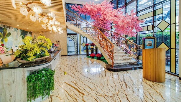 Un vestíbulo con piso de mármol, una recepción, una escalera adornada con flores artificiales rosas y un atril de madera.