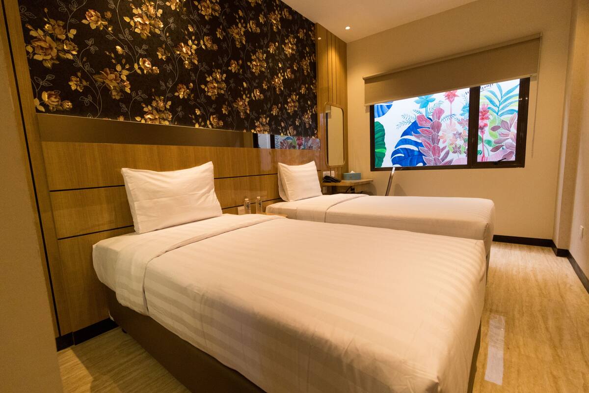 A hotel room with two beds, a large mirror, and a floral wallpaper.