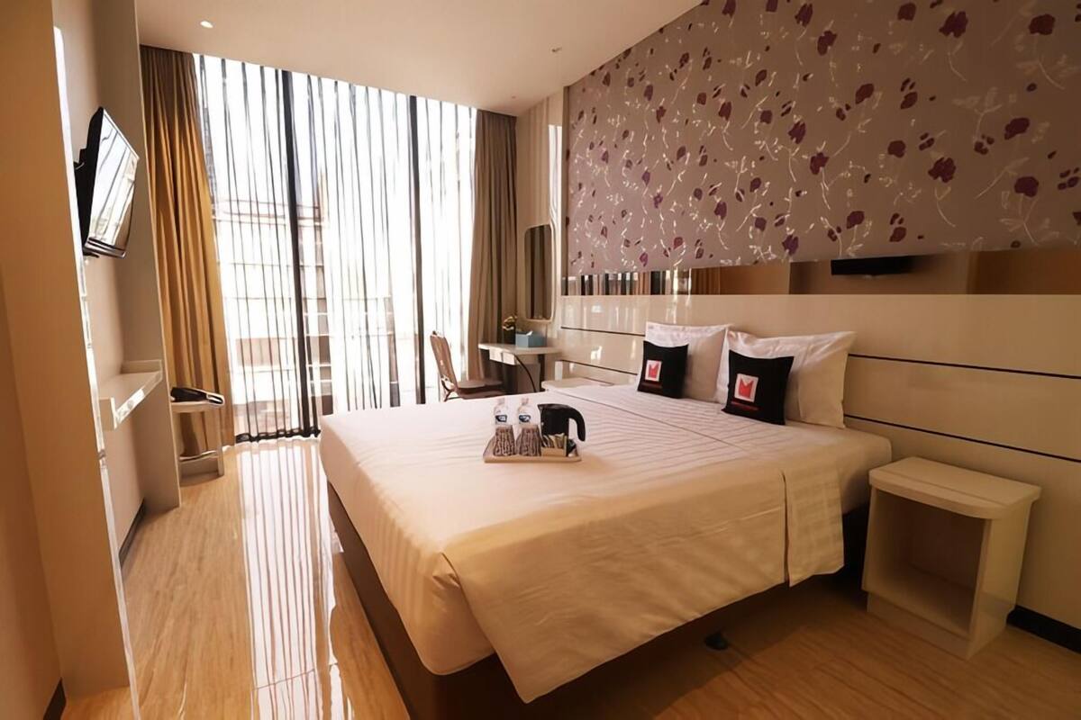 A hotel room with a large bed, a bedside table, a chair, a desk, and a large window with curtains.