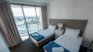 A hotel room with two beds, a nightstand, a lamp, and a view of a cityscape through large windows. - Chevron Renaissance-Resort Style Living managed by Gold Coast Premium (Surfers Paradise)