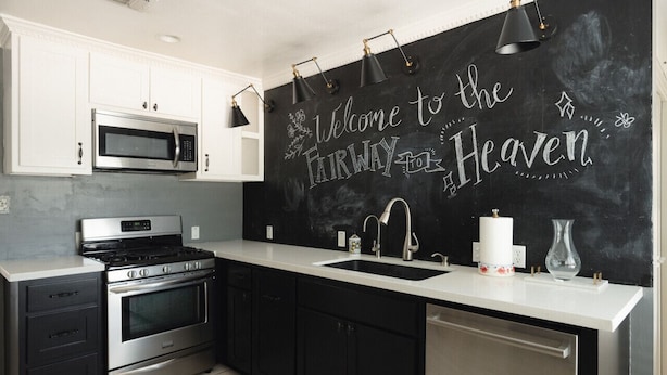 A modern kitchen with white cabinetry, stainless steel appliances, and a chalkboard wall with "Welcome to the Farway Heaven" written on it. - The Fairway to Heaven (Bryan)