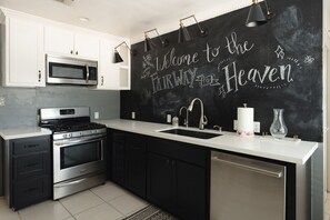 A modern kitchen with white cabinetry, stainless steel appliances, and a chalkboard wall with "Welcome to the Farway Heaven" written on it. - The Fairway to Heaven (Bryan)