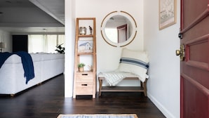 A hallway with a wooden bench, a small wooden shelf with decorative items, a round mirror, and a red door. - The Fairway to Heaven (Bryan)