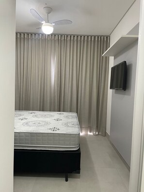 Ein Schlafzimmer mit Bett, Deckenventilator, an der Wand montiertem Fernseher und einem mit Vorhängen versehenen Fenster.