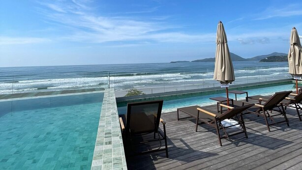 Una piscina a sfioro con vista sull'oceano, un pontile in legno e sedie a sdraio con ombrelloni.