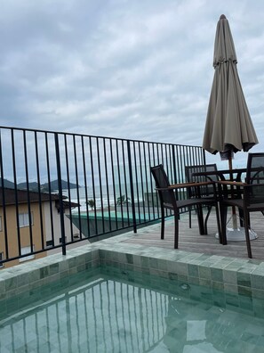 Ein Poolbereich mit Blick auf den Ozean, ein Tisch mit Stühlen und ein Sonnenschirm.