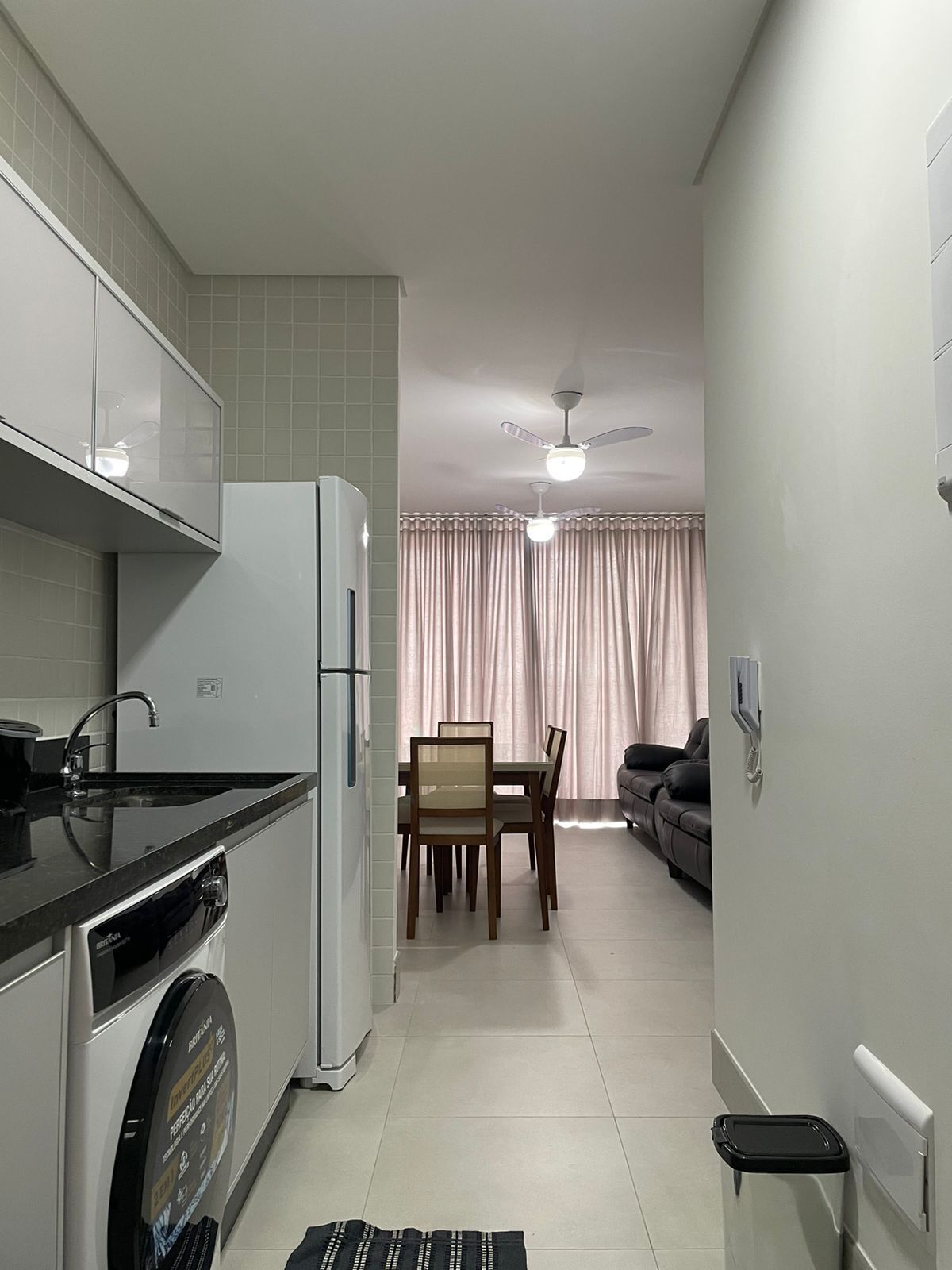A compact kitchen with a refrigerator, washing machine, and a dining area with a table and chairs.