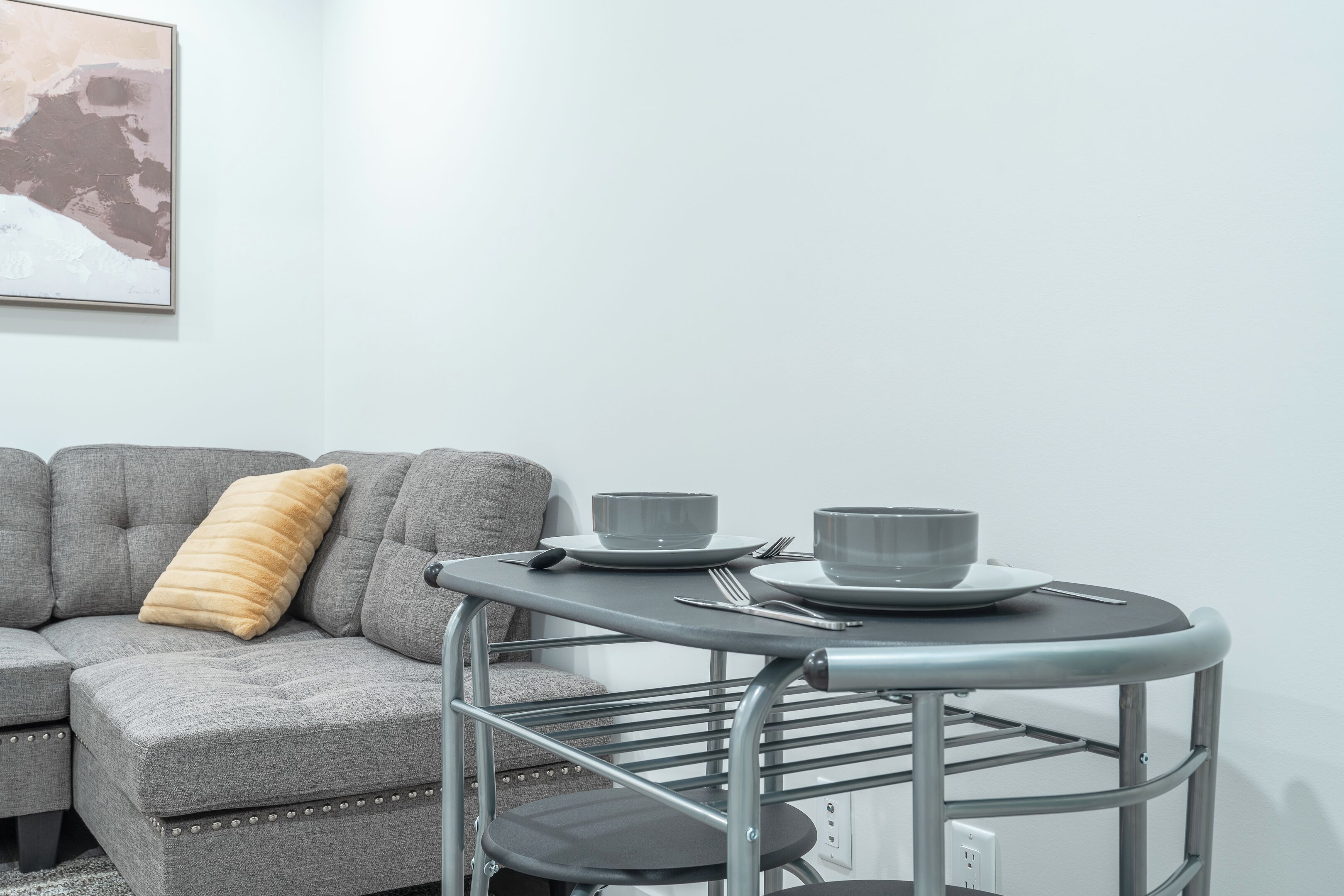 Ein modernes Wohnzimmer mit einem grauen Sofa, einem kleinen runden Tisch mit Schüssel und Tasse sowie einem grauen Sessel.