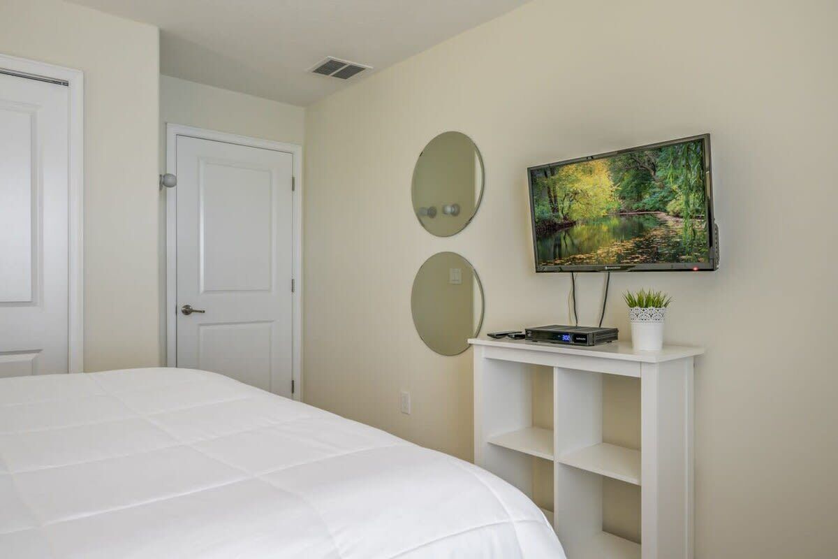 Une chambre à coucher avec un lit, un téléviseur fixé au mur et une petite étagère blanche sur laquelle est posée une plante.