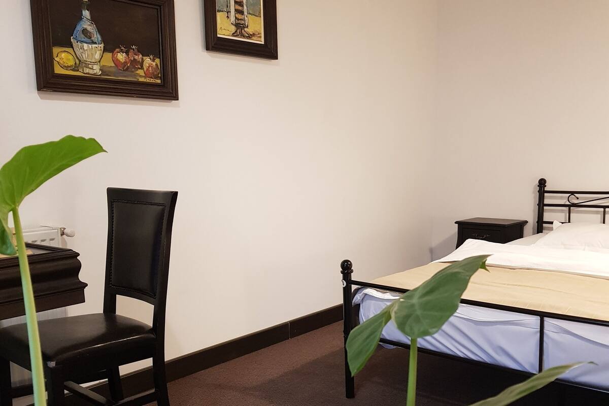 Quarto com uma cama, uma cadeira, uma mesinha de cabeceira e duas obras de arte emolduradas na parede.