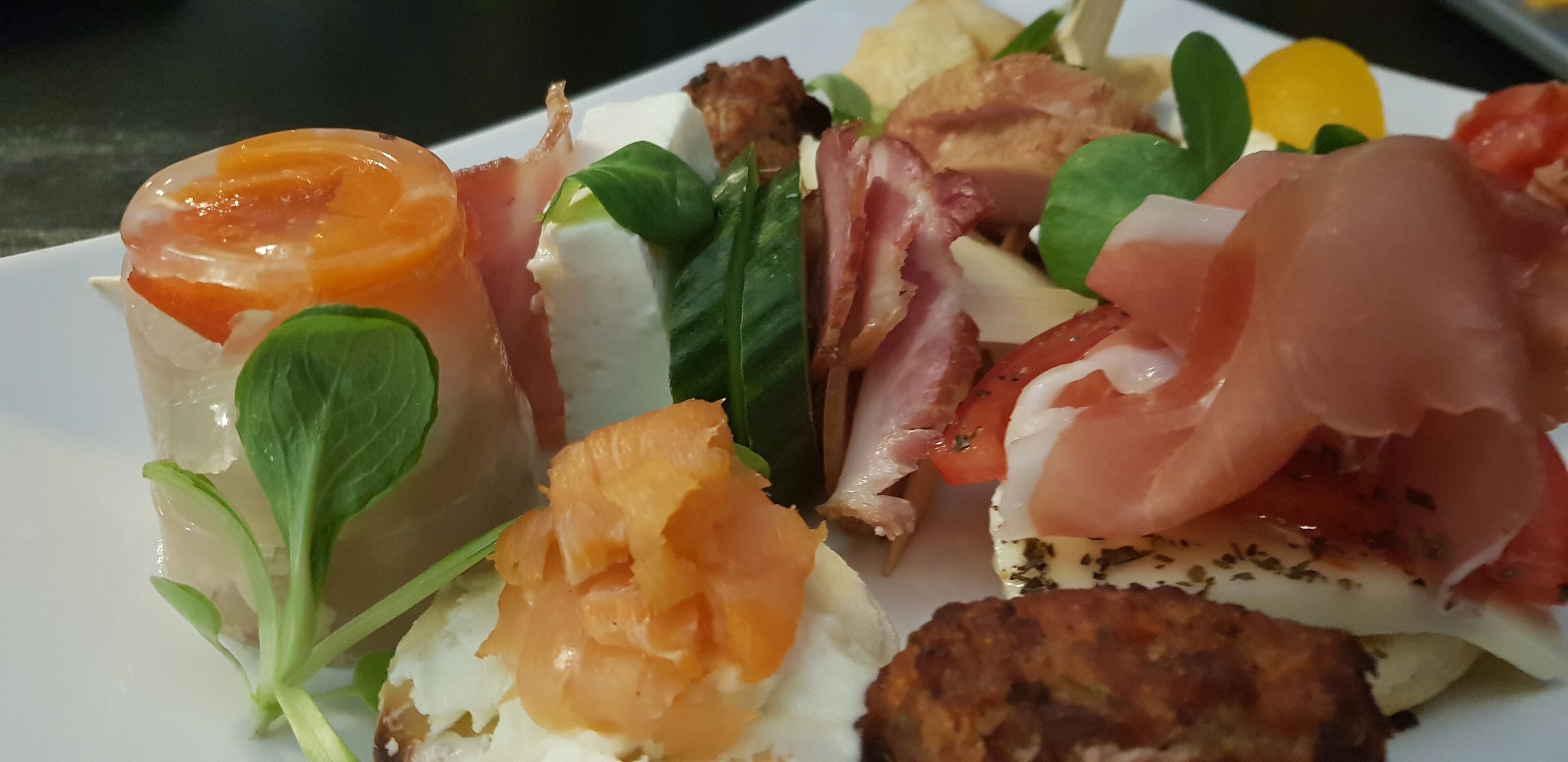 Un plato con una variedad de alimentos, incluyendo salmón ahumado, prosciutto y otros ingredientes.