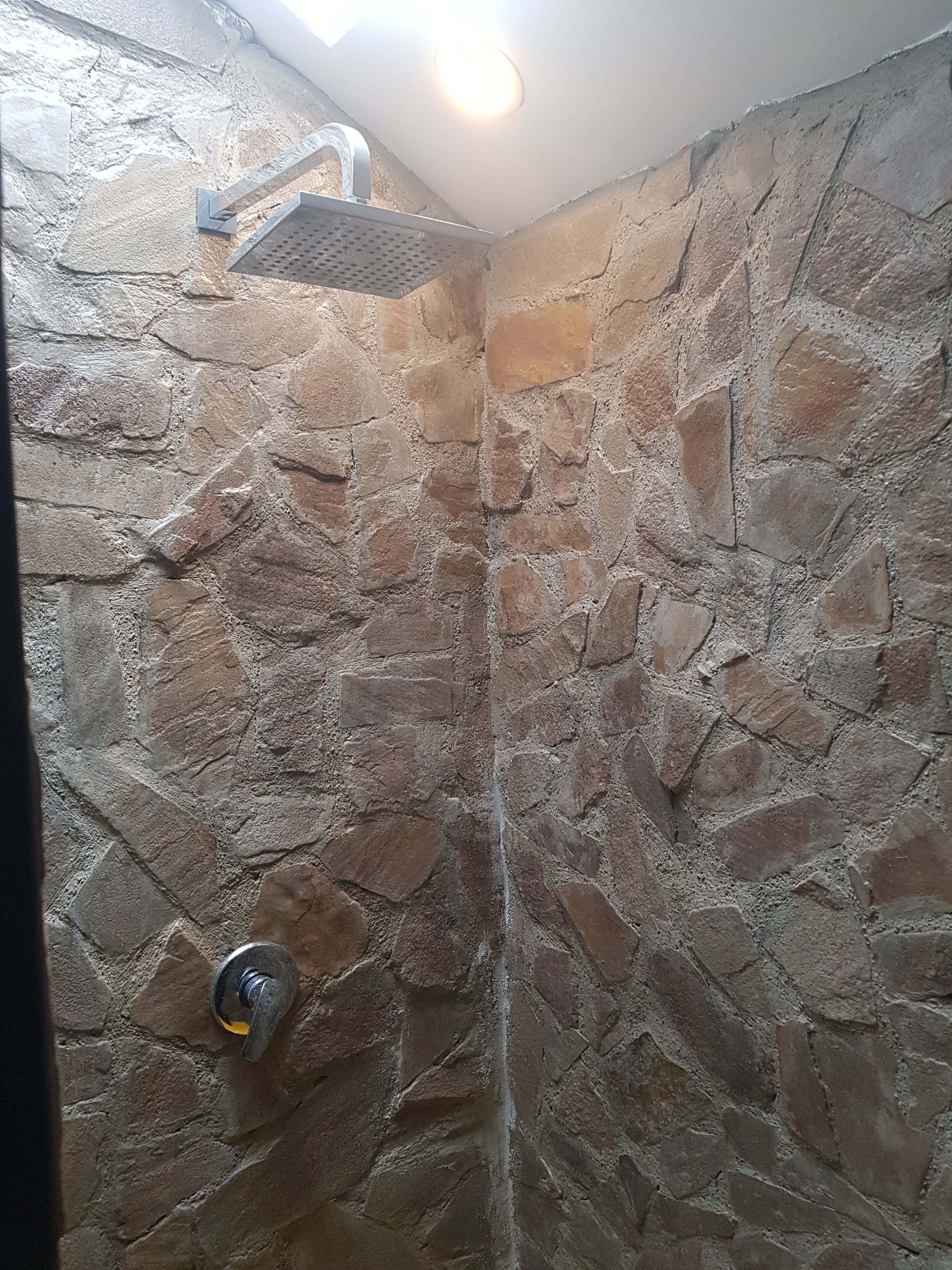 Cabina doccia in pietra con soffione a pioggia integrato e doccetta manuale.