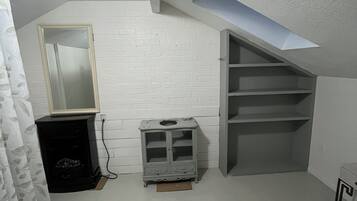 Una habitación con techo inclinado, pared de ladrillo blanco, un mueble pequeño, un espejo y una estantería.