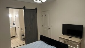 Et soveværelse med en seng, et fjernsyn på et lille bord, en dør og en loftlampe.