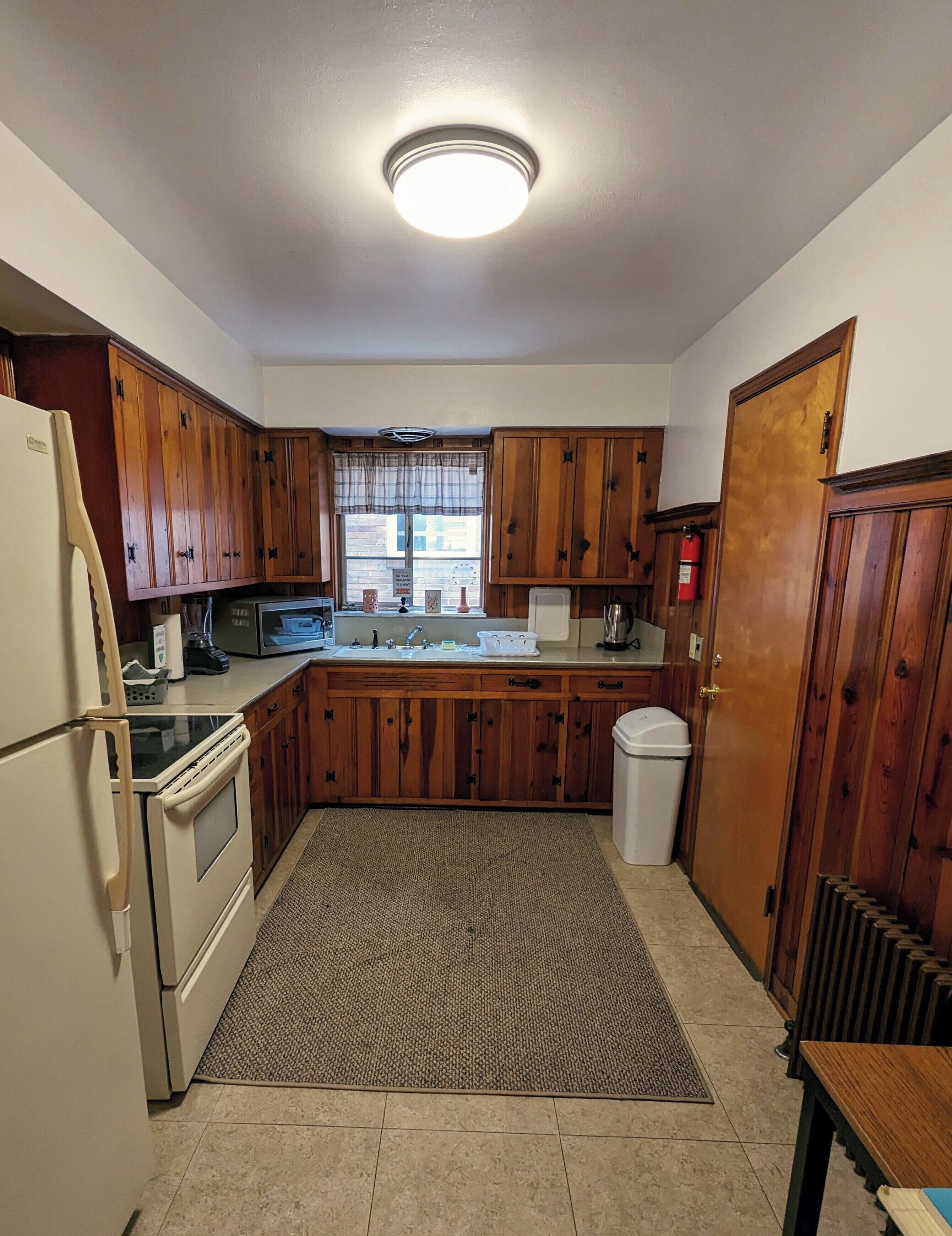 A kitchen with wooden cabinets, a refrigerator, a stove, a microwave, and a window with a view of the outside.