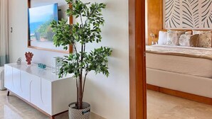 A modern hotel room with a large bed, a TV mounted on a white cabinet, and a potted plant. - Luxurious, Stunning Bay View Condo, King Bed, Spacious Terrace, Pool, Gym. (Samaná)
