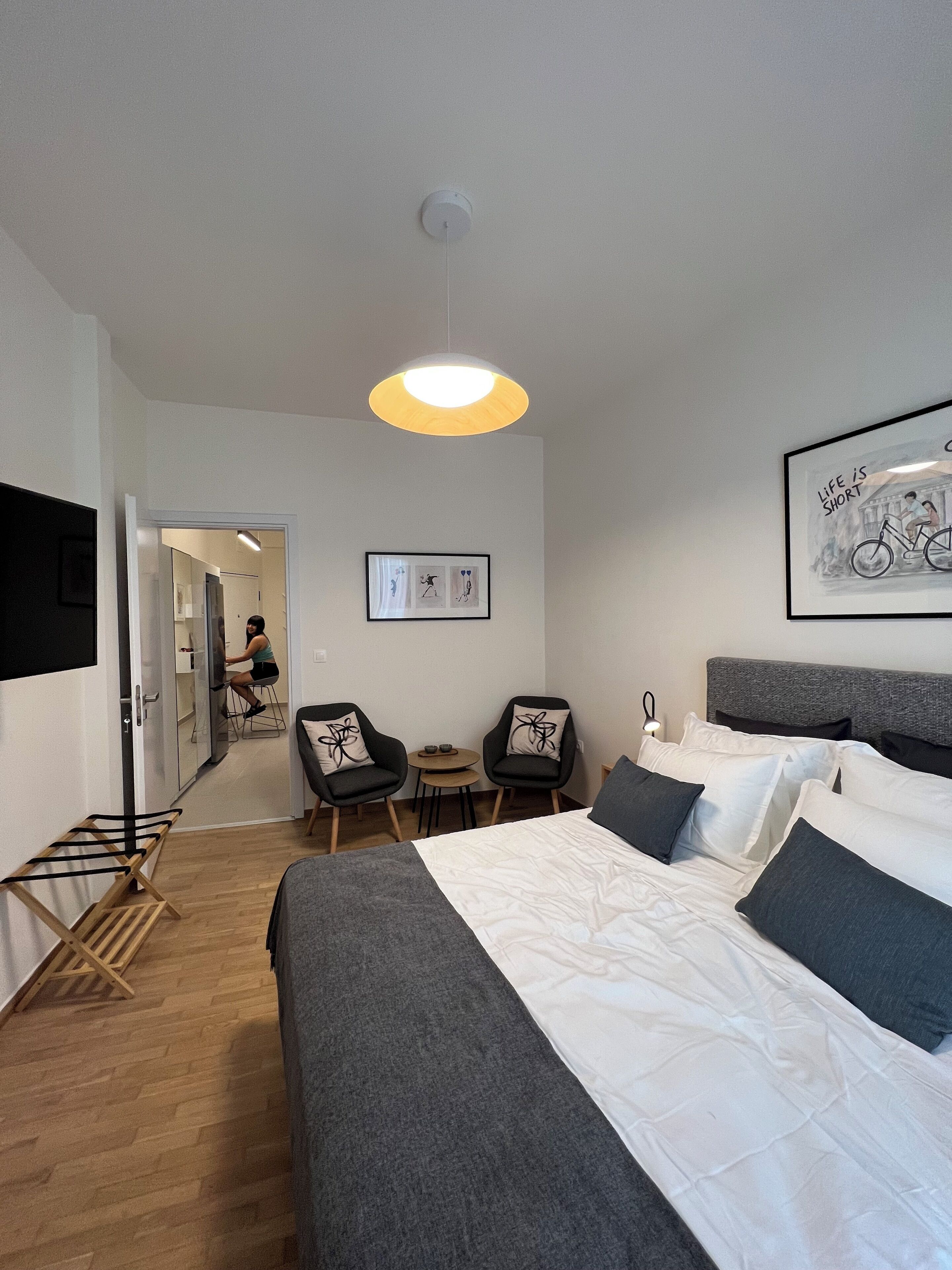Een moderne hotelkamer met een groot bed, twee fauteuils, een tafeltje en een wanddecoratie.