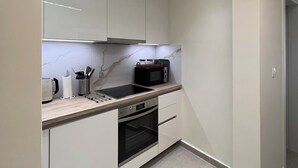 A modern kitchen with white cabinets, a microwave, a toaster, and a kettle. - Stylish 1BR Apt. Opposite Metro- Balcony & Rooftop Lounge with Acropolis View (Athina)