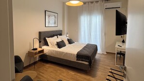 A modern bedroom with a bed, bedside table, lamp, and a desk with a chair. - Stylish 1BR Apt. Opposite Metro- Balcony & Rooftop Lounge with Acropolis View (Athina)