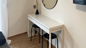 A small, modern room with a white desk, two black stools, a round mirror, and an air conditioning unit on the wall. - Stylish 1BR Apt. Opposite Metro- Balcony & Rooftop Lounge with Acropolis View (Athina)