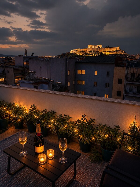 A rooftop terrace with a table set for two, a bottle of wine, and candles.