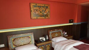 A hotel room with two beds, a wooden headboard, a wall-mounted painting, and a bedside table with a phone and a kettle. - Hotel De Purang (Muktinath)