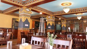 A restaurant with wooden tables and chairs, decorative ceiling patterns, and chandeliers. - Hotel De Purang (Muktinath)