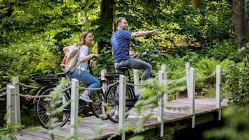 Dues persones amb bicicleta sobre un pont de fusta envoltades de vegetació.