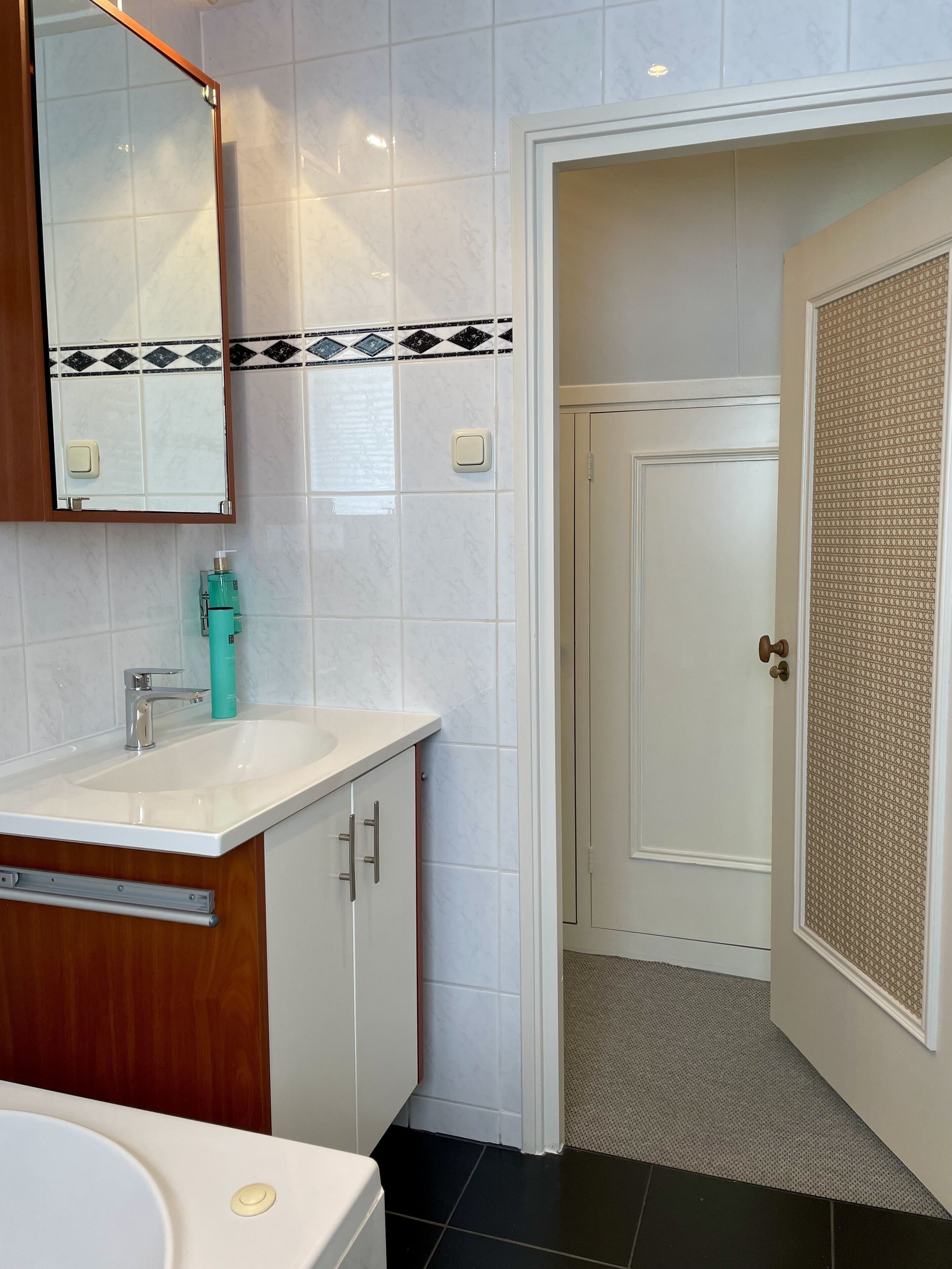 A bathroom with a white sink, mirror, and cabinet, a toilet, and a door with a patterned panel.