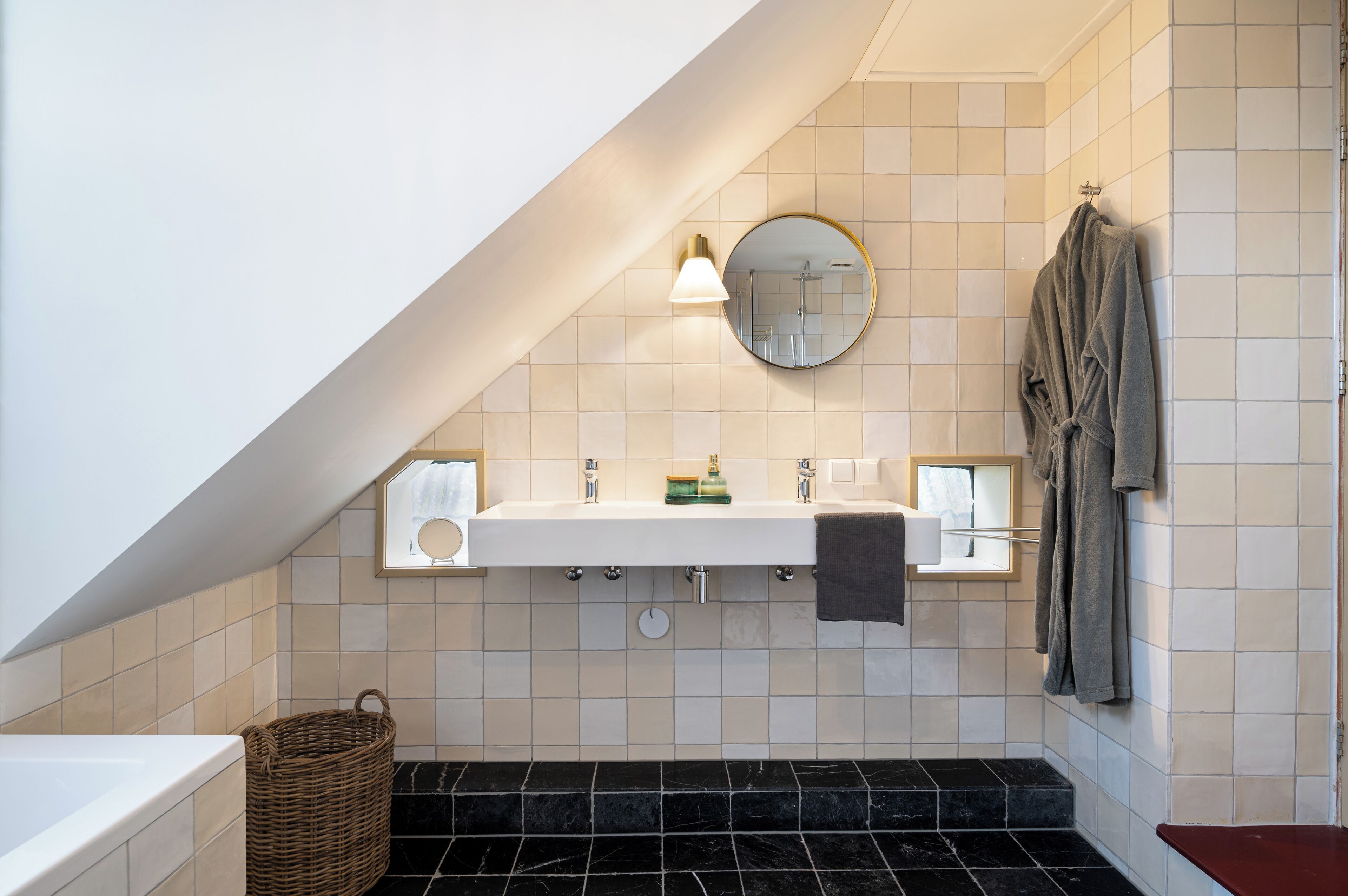 Een moderne badkamer met een wit wastafelmeubel, een ronde spiegel en een handdoekrek.