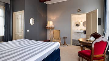 Ein Hotelzimmer mit Bett, Sessel, Tisch, Lampe und einem durchgehenden Türspalte sichtbaren Badezimmer.